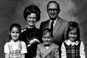 Black and white photo of family of five, dressed formally and smiling.