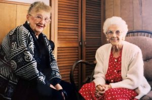 Color photo of two smiling older women wearing cardigans