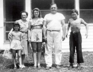 Historical black and white photo of a family of five, standing and smiling, in informal warm-weather clothes.