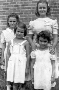 Historical black and white photo of four girls in standing together in white summer dresses.
