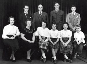 Black and white photo of family of 10, dressed formally. Front row is seated and back row is standing.