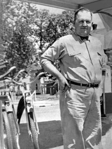 A man standing and smiling with his hands on his hips next to three bicycles.