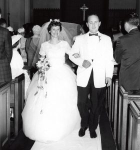 Black and white photo of a smiling bride and groom walking down the aisle.