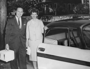 Black and white photo of a formally dressed couple standing next to a car with the door open.